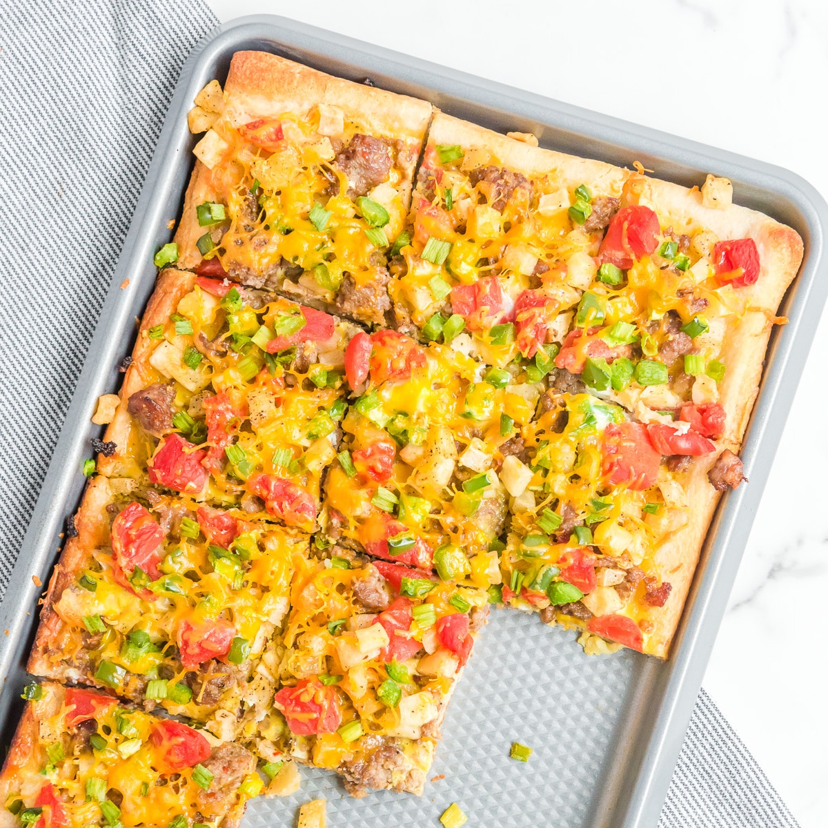 Up close of a rectangular sausage breakfast pizza on a pan from overhead missing a few pieces on the pan.