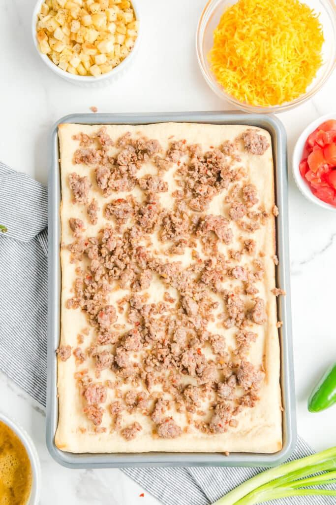 Sausage spread across the pizza dough on a baking sheet from above.