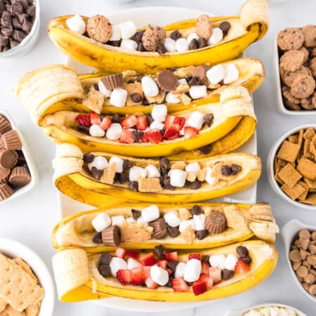 Square view of six banana boats filled with chocolate, marshmallows, graham crackers, strawberry pieces and mini peanut butter cups from above.