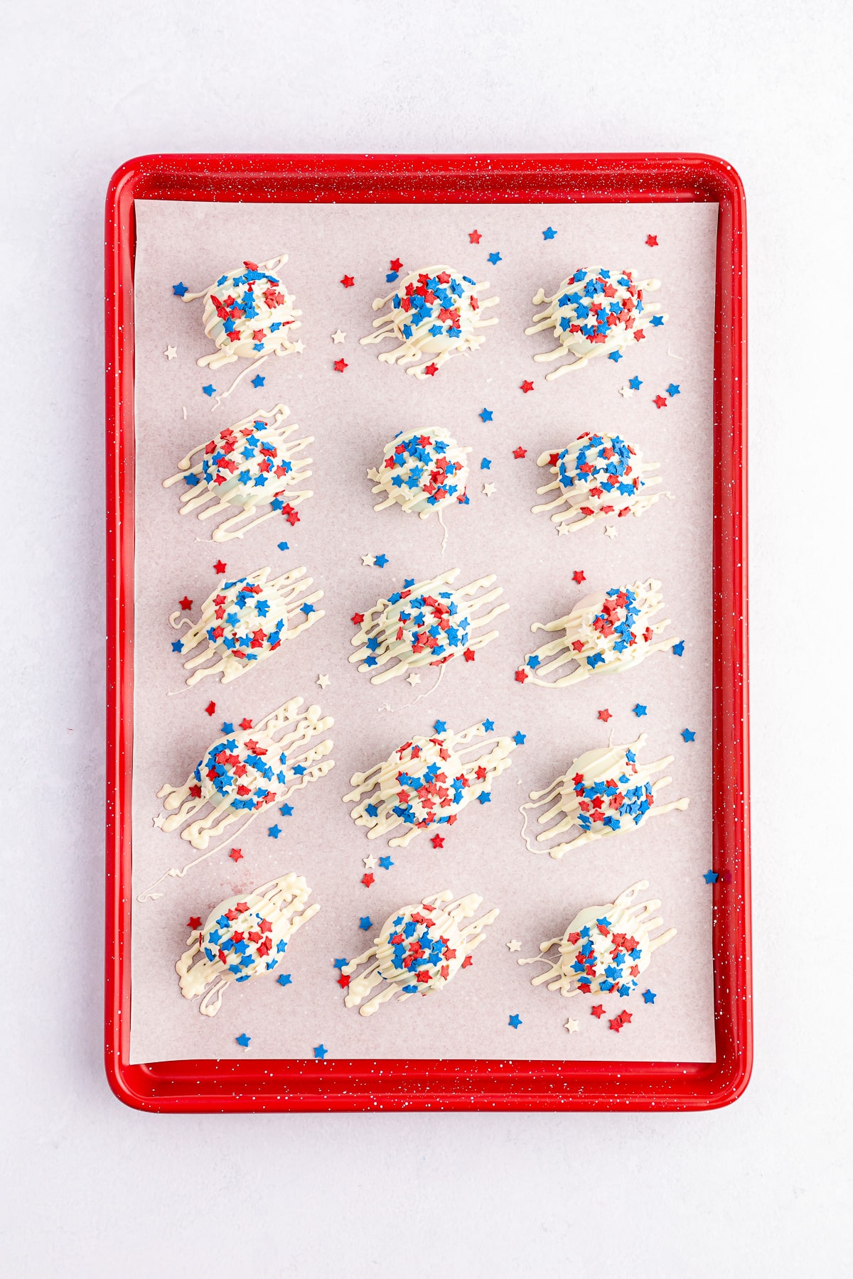 Cake balls coated in white chocolate and red and blue sprinkles from overhead on a baking sheet.