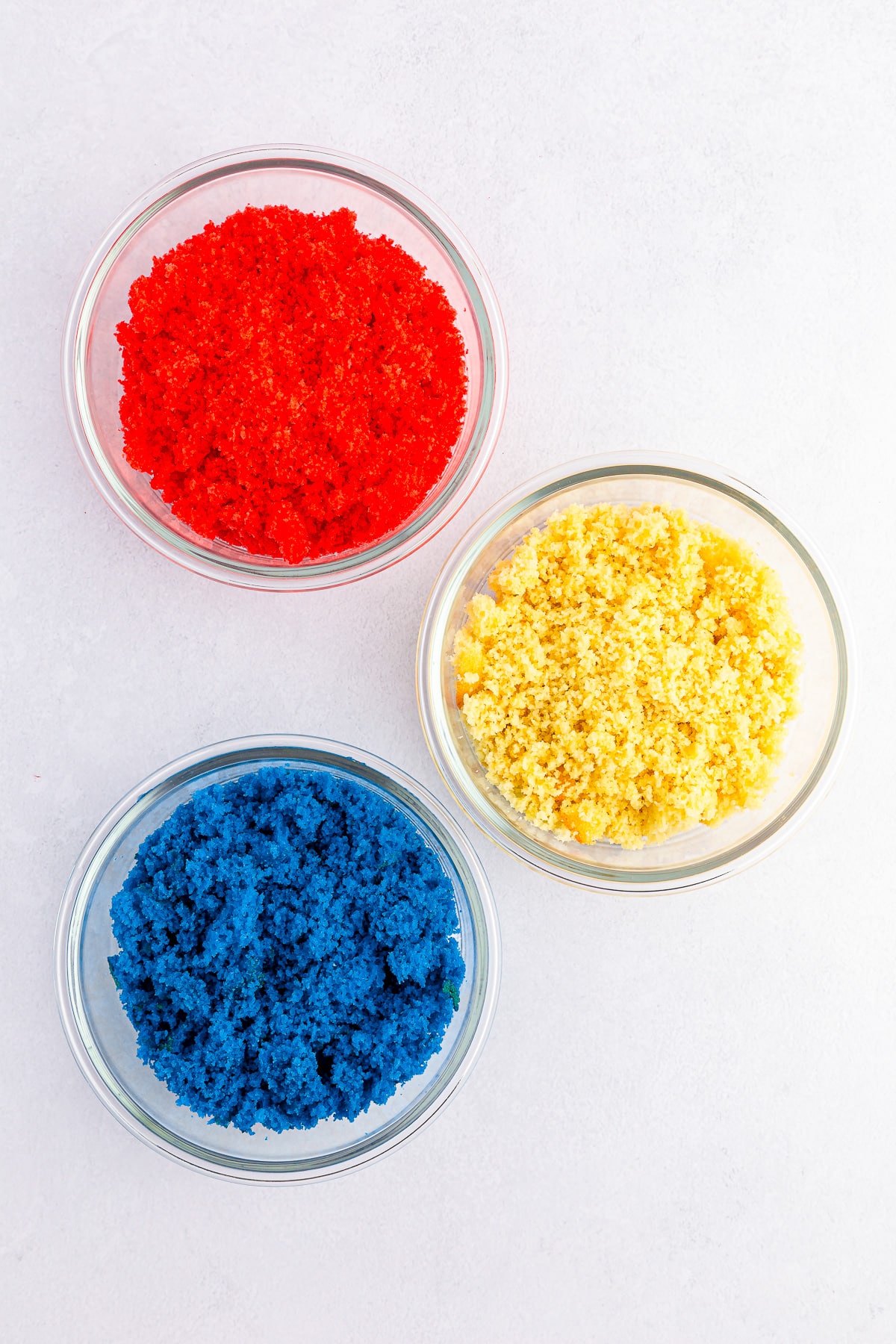 Colored cake crumbled in individual bowls of red, white and blue crumbs from overhead.