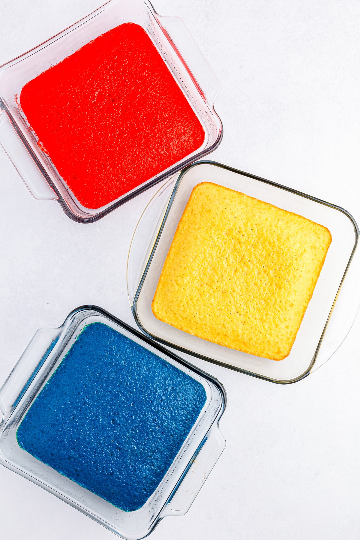 Three cakes cooked in square glass pans from overhead, one red, one white and one blue.