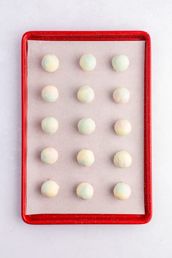 Cake balls dipped in white chocolate on a lined baking sheet from overhead.
