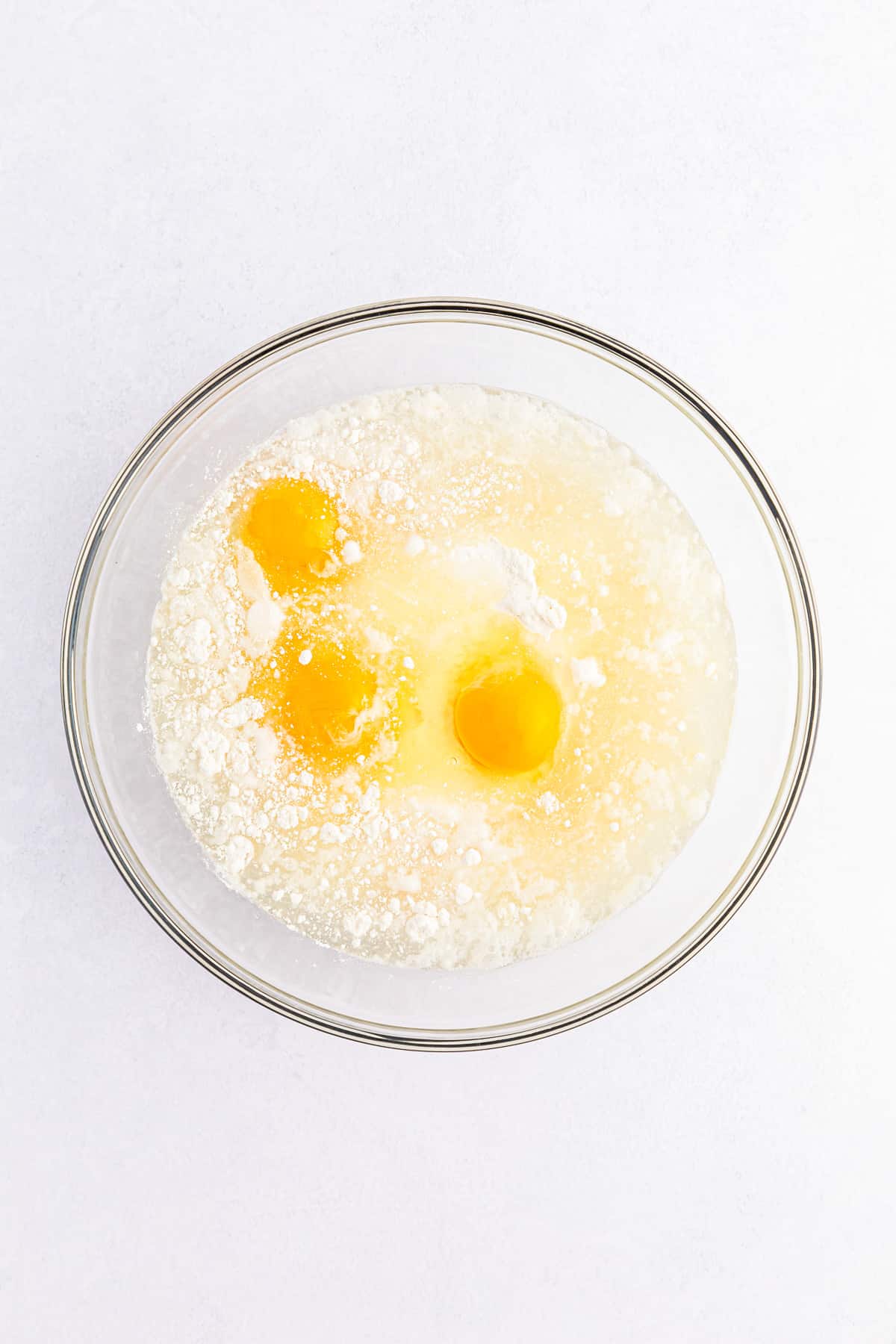 Eggs and oil in a bowl being mixed into white cake mix from overhead.