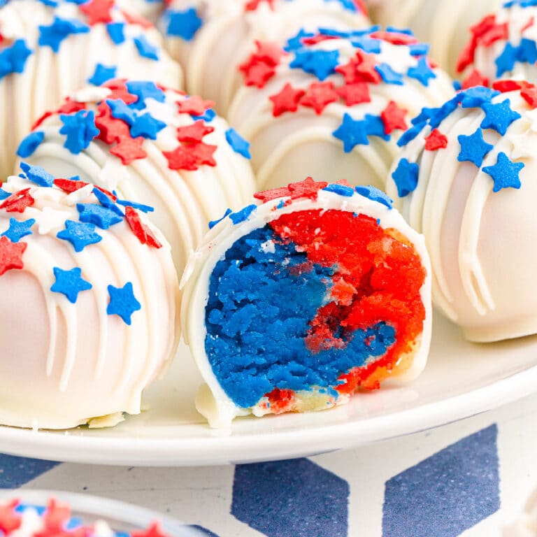 Close up of the inside of a red and blue cake ball next to more cake balls on a plate covered in red and blue star sprinkles and white chocolate.