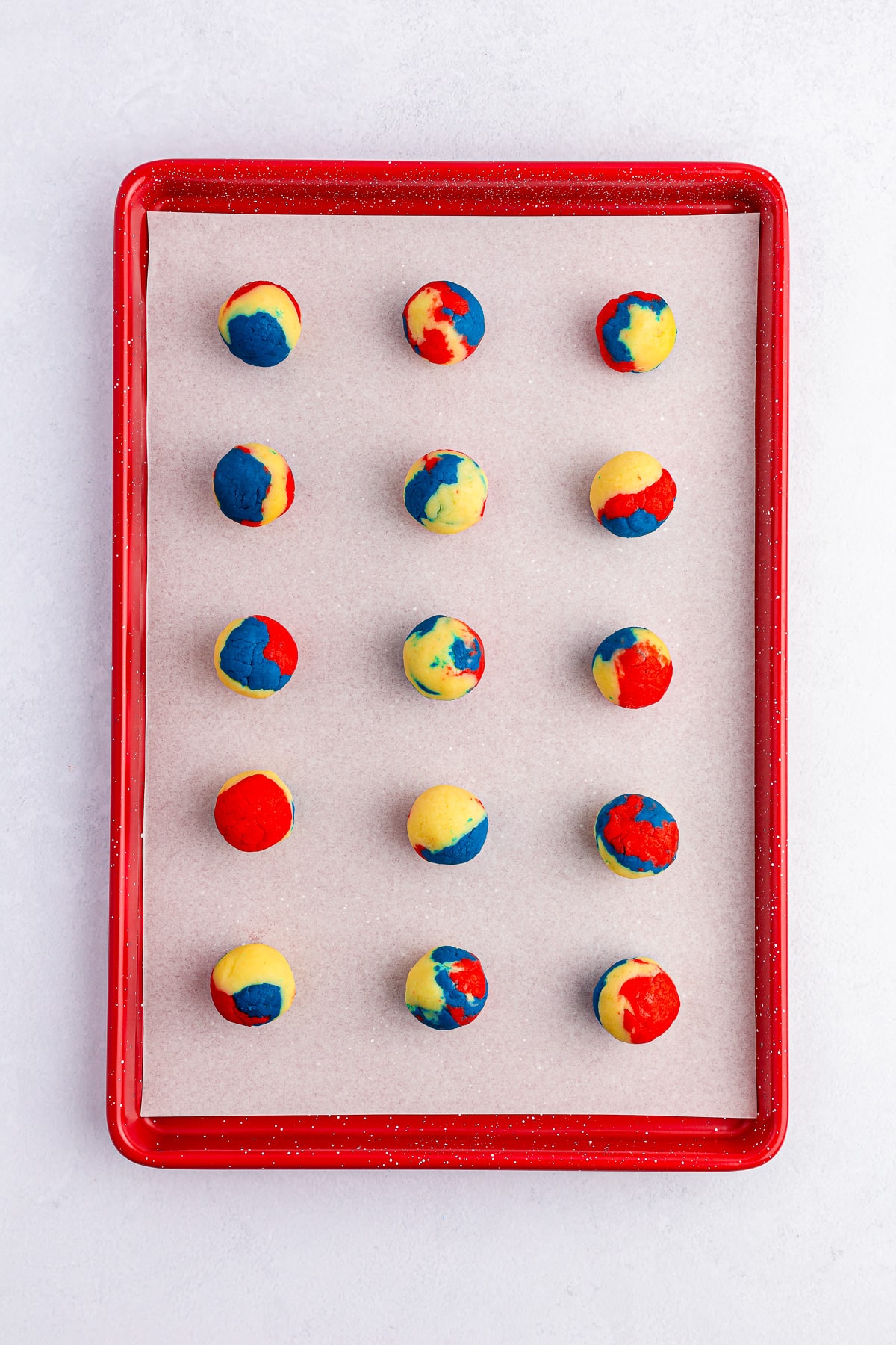 Red white and blue cake rolled together into cake balls on a baking sheet from overhead.