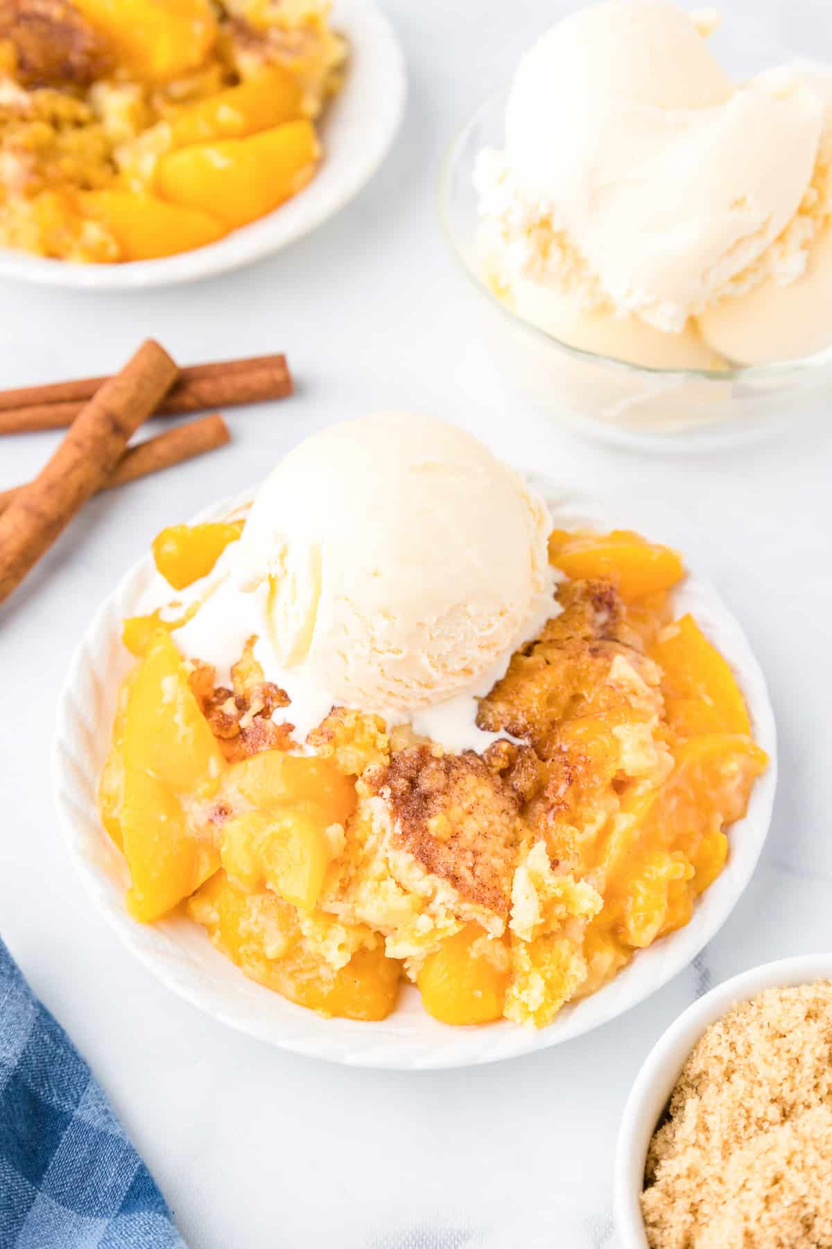 Peach dump cake on a plate from an angle topped with vanilla ice cream on a counter.