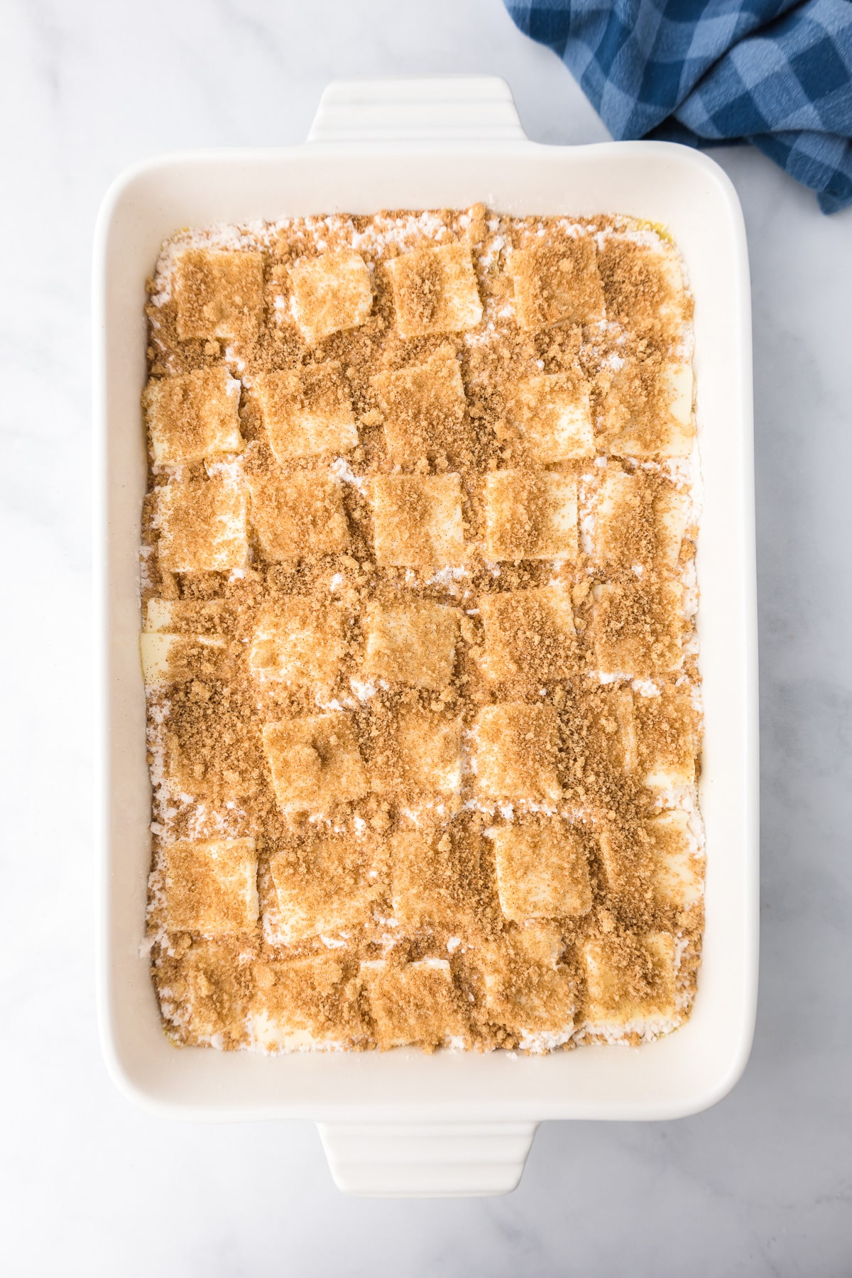 Cinnamon sugart layered over pats of butter, cake mix and peaches in a pan from overhead on a counter in a large rectangular baking dish.