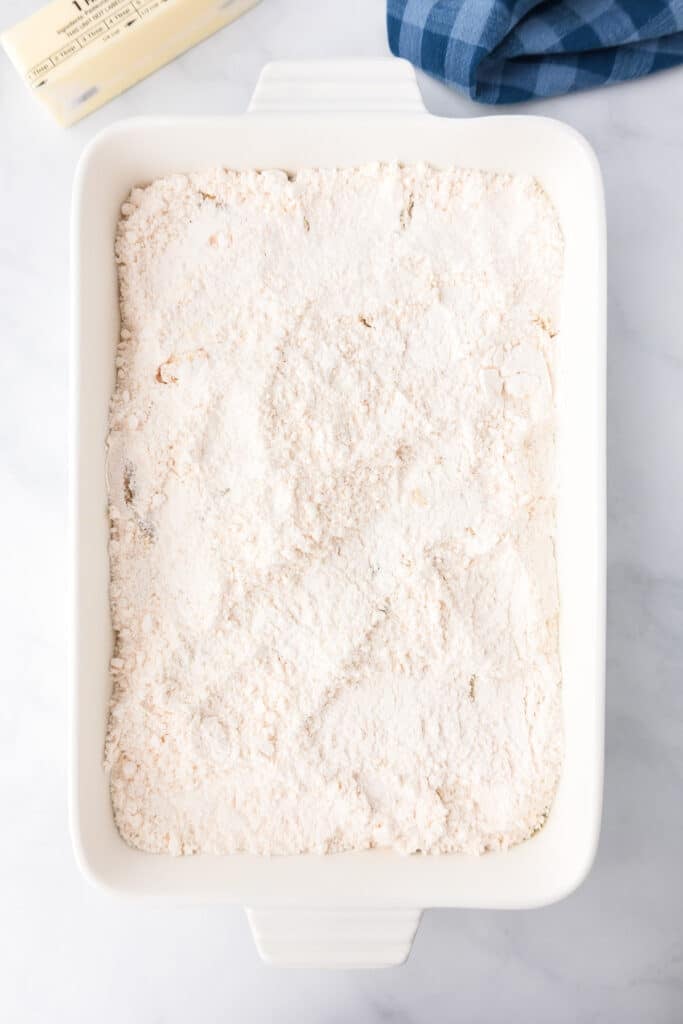 Cake mix layered over peaches in a large rectangular baking dish on a counter.
