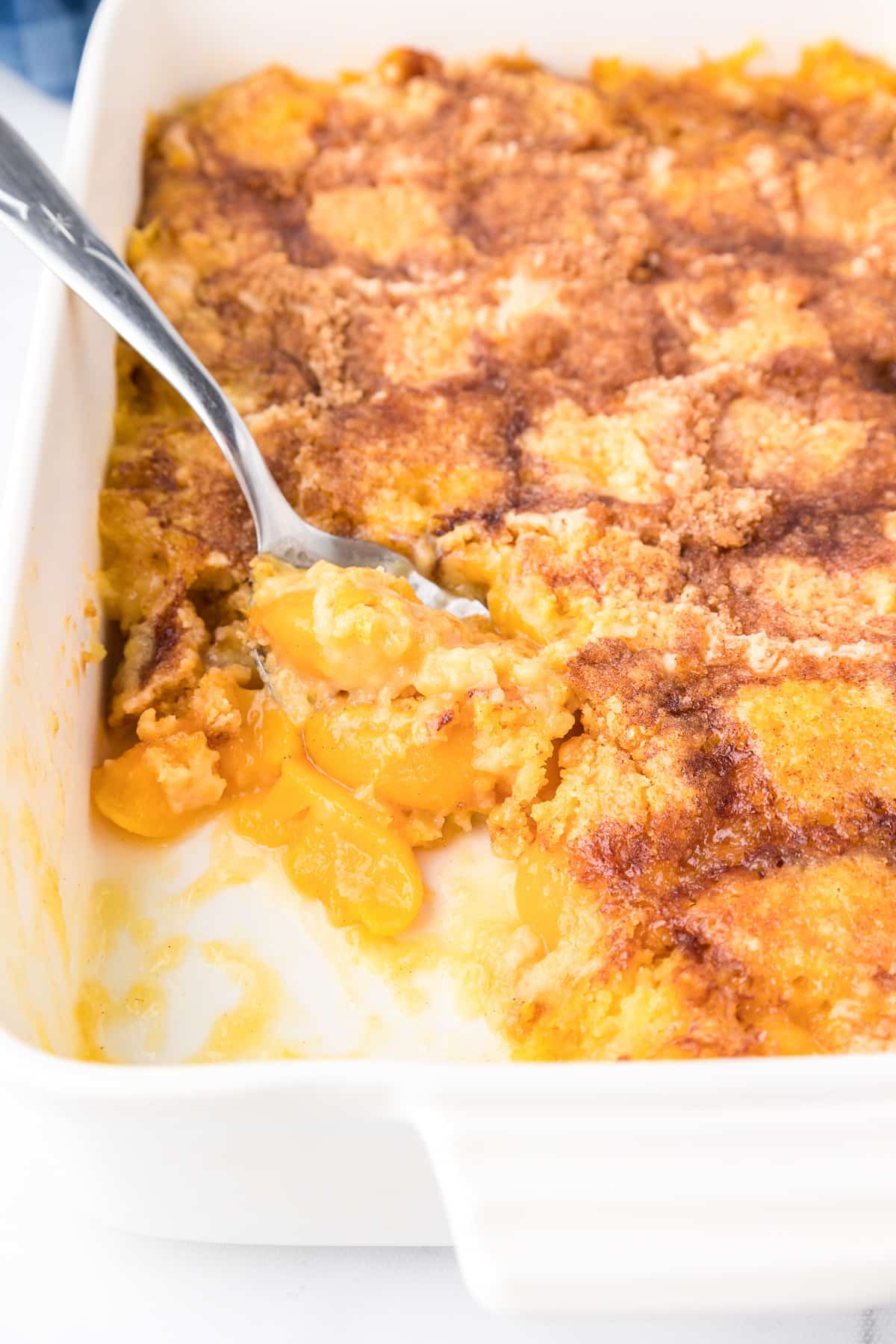 Peach dump cake close up in a pan being scooped by a spoon with a scoop missing.