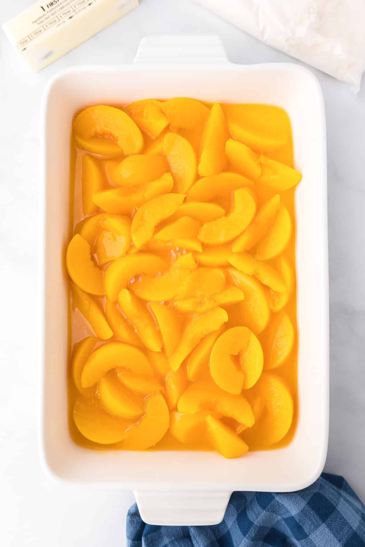Peaches in juice in a large rectangular baking dish from overhead on a counter.