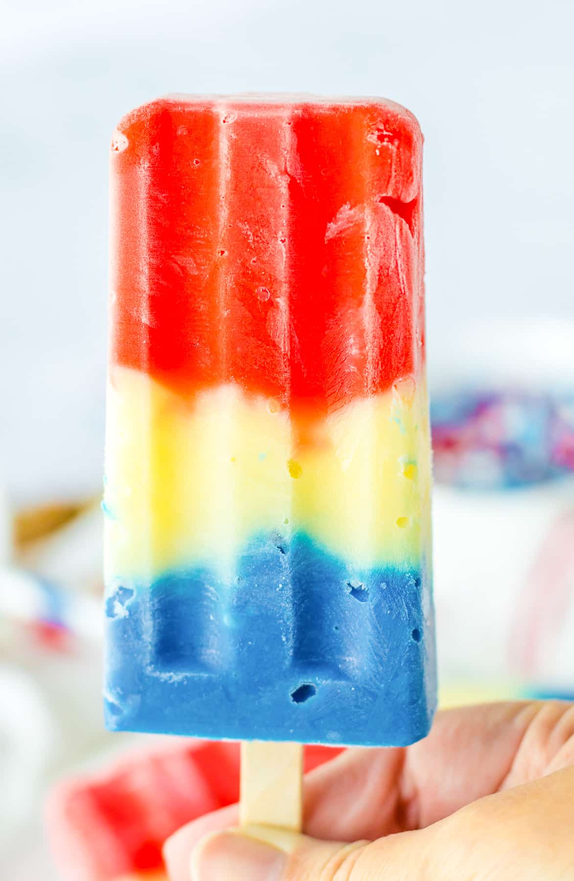 A red, white and blue popsicle being held up by a hand.