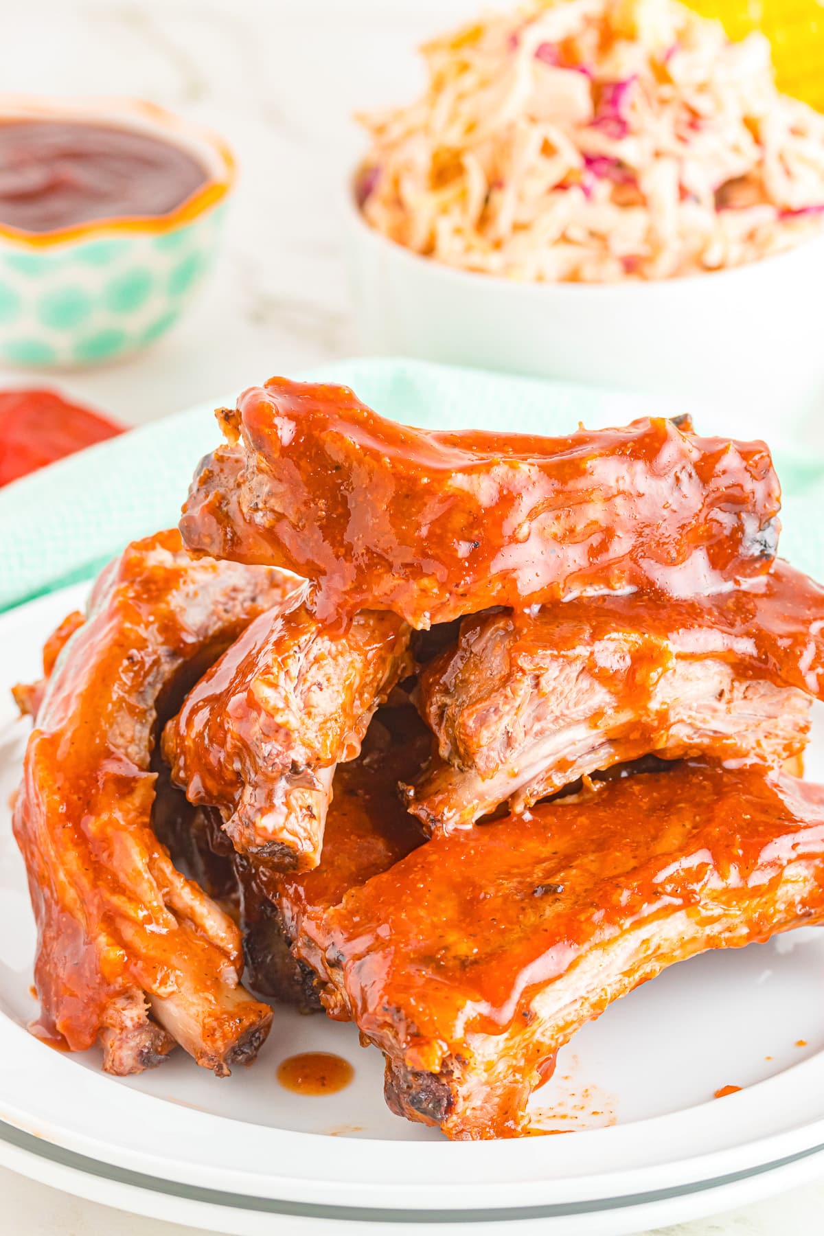 Saucy Dr. Pepper Ribs piled high on a plate from the side with side dishes in the background.