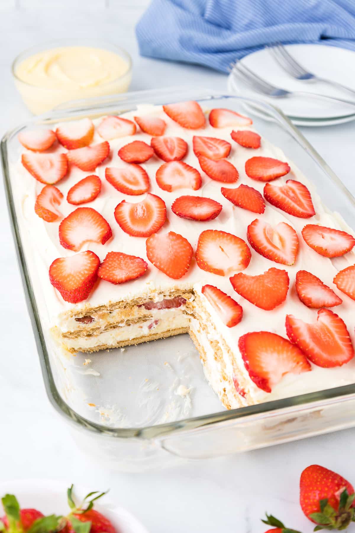 An entire pan of strawberry cream cheese icebox cake with an angled view missing a slice allowing you to see the layers in the cake.