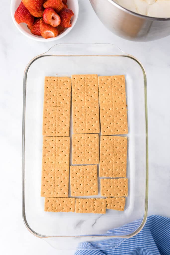 Graham crackers layered in the bottom of a large rectangular glass pan on a counter from overhead.