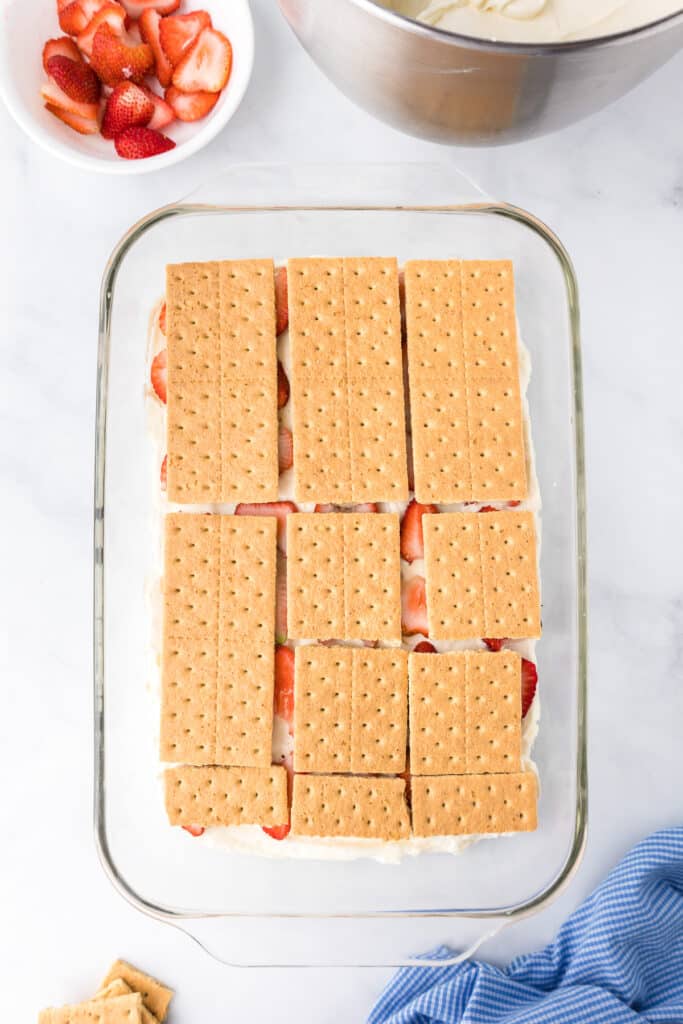 Graham crackers layered on top of strawberries and cream in a large rectangular glass pan.