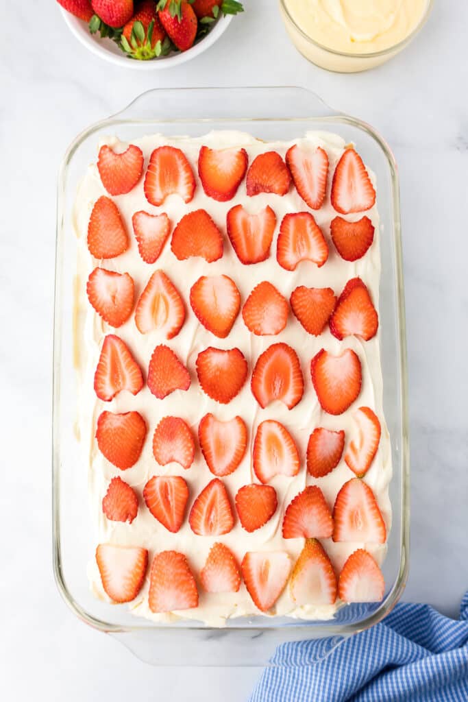 Sliced strawberries layered on top of the cream in the icebox cake in a large glass rectangular pan.