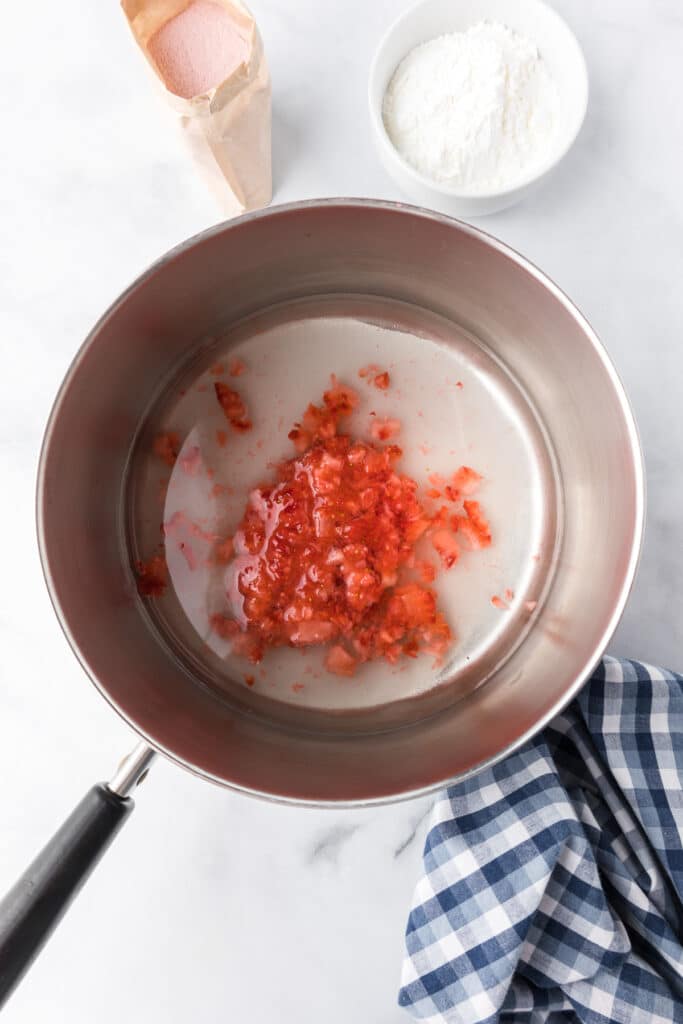 Diced mashed strawberries being mixed in a pan with sugar and strawberry gelatin.