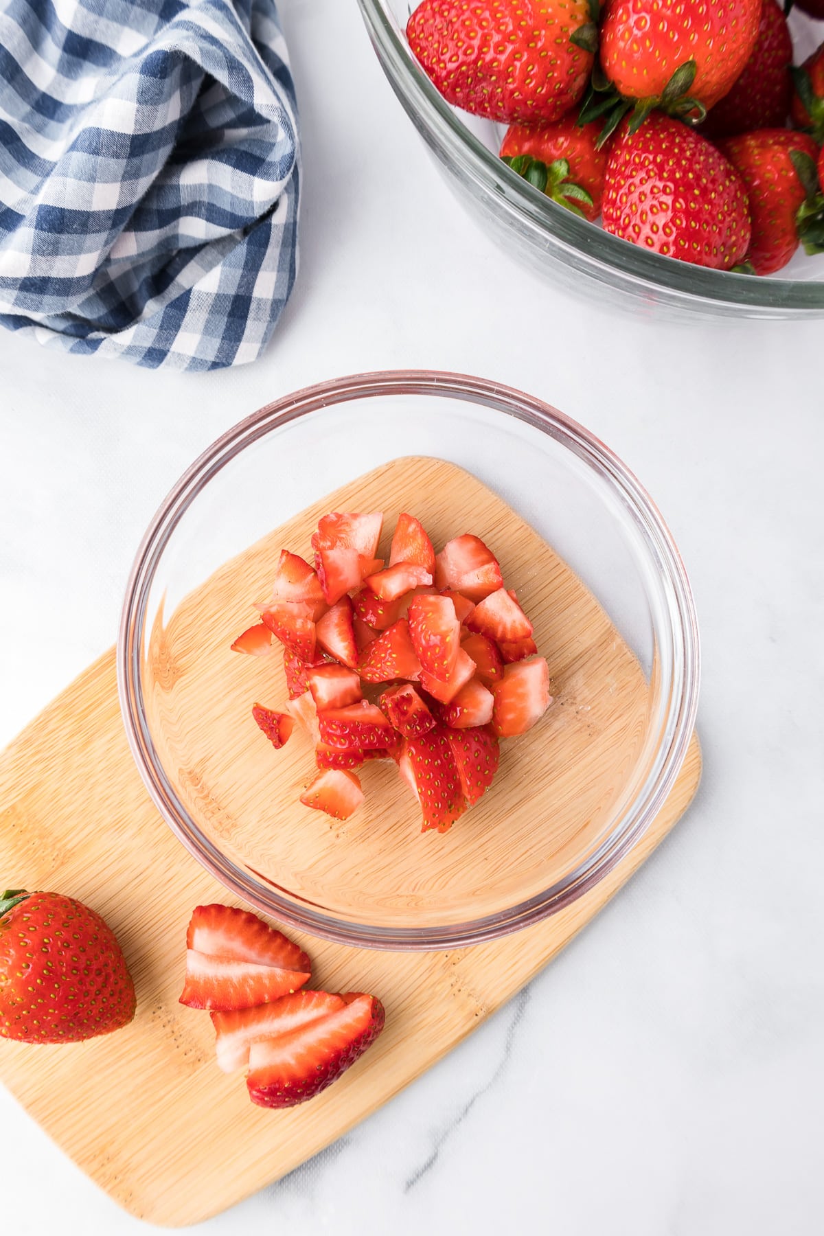 Strawberries being diced and placed in a bowl on a cutting board form overhead on a counter.