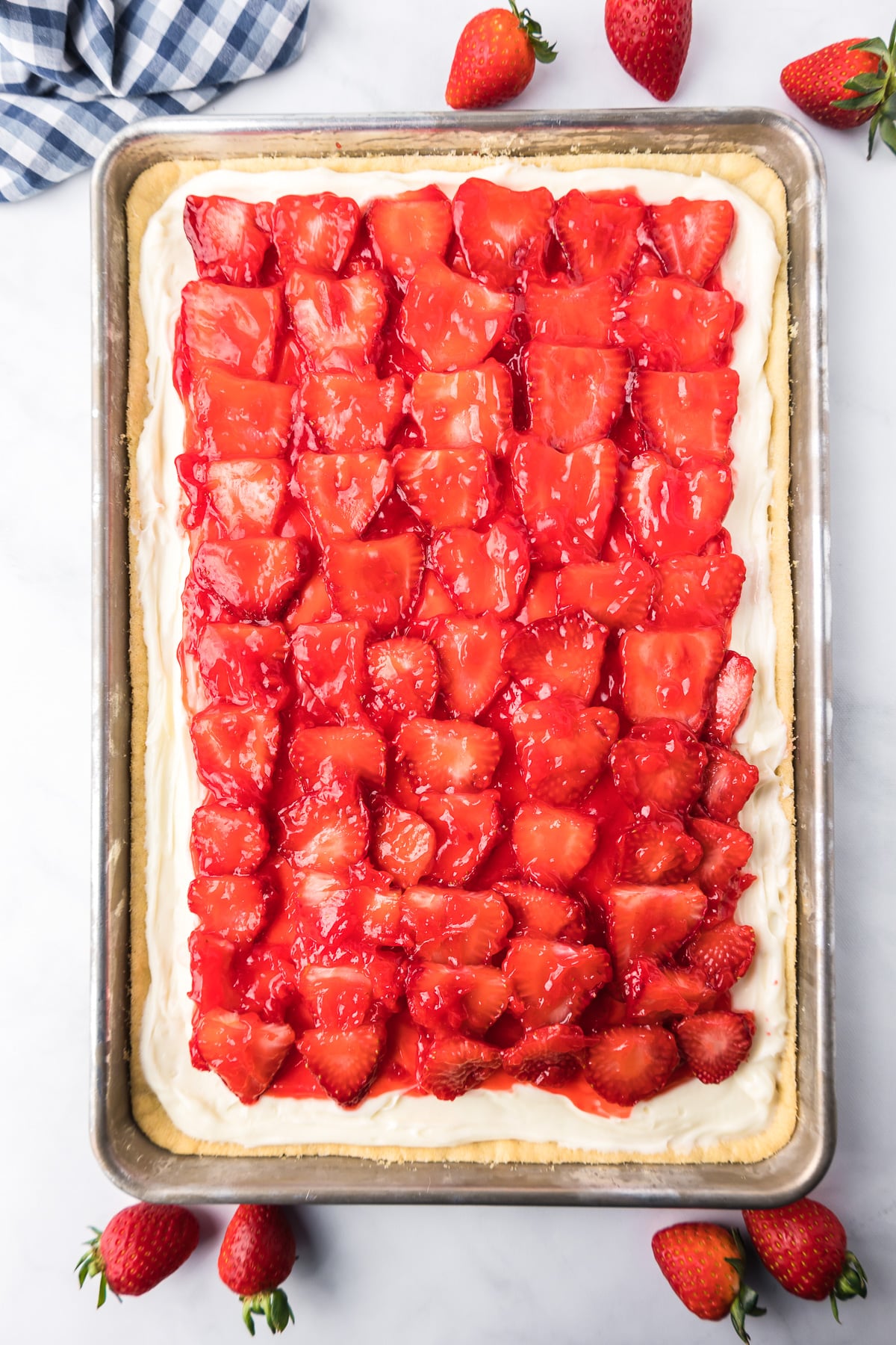 Finished strawberry pizza on a sheet pan topped with glazed strawberries from overhead on a counter after chilled.