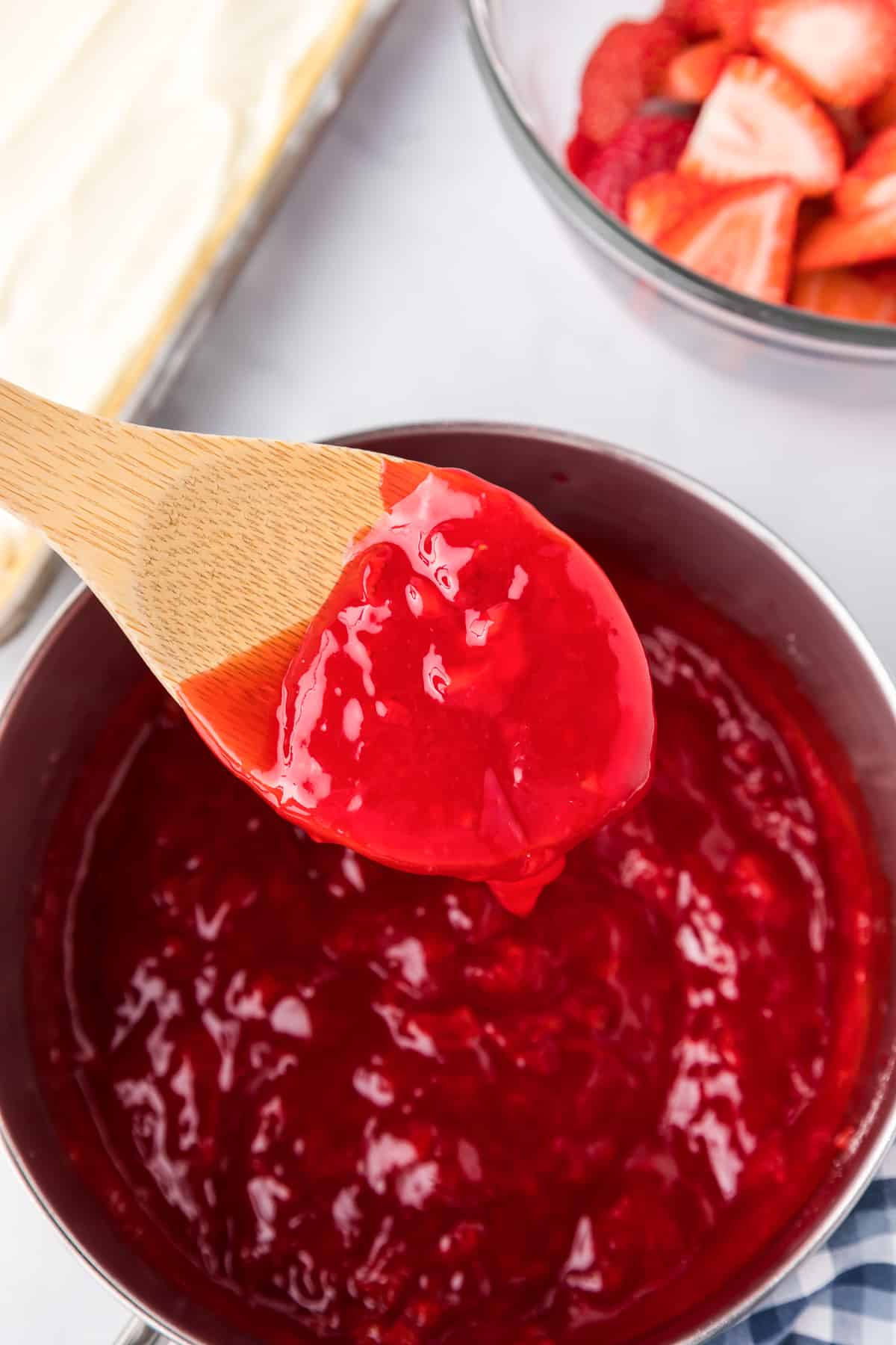 Thick strawberry sauce being lifted from the pan with a wooden spoon.