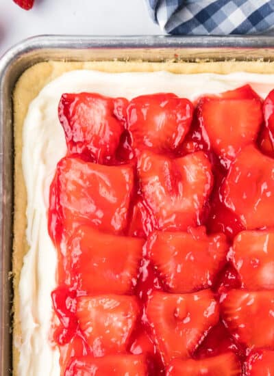 Strawberry pizza with a cookie dough, frosting and glazed strawberries from above showing most of a sheet pan on a counter.
