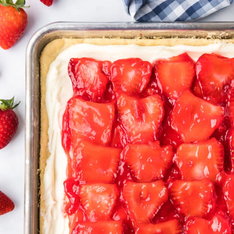 Strawberry pizza with a cookie dough, frosting and glazed strawberries from above showing most of a sheet pan on a counter.