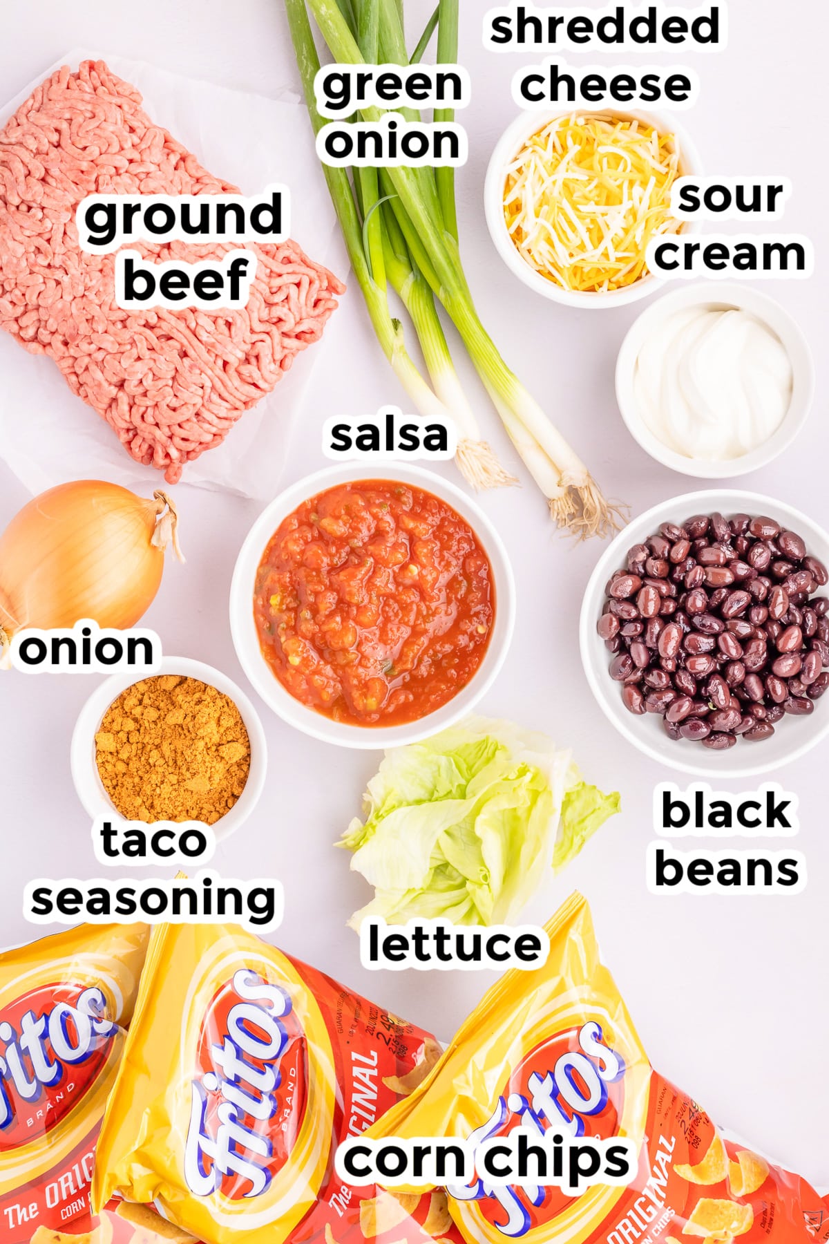 Ingredients for walking tacos on a counter from overhead in bowls with text labels.