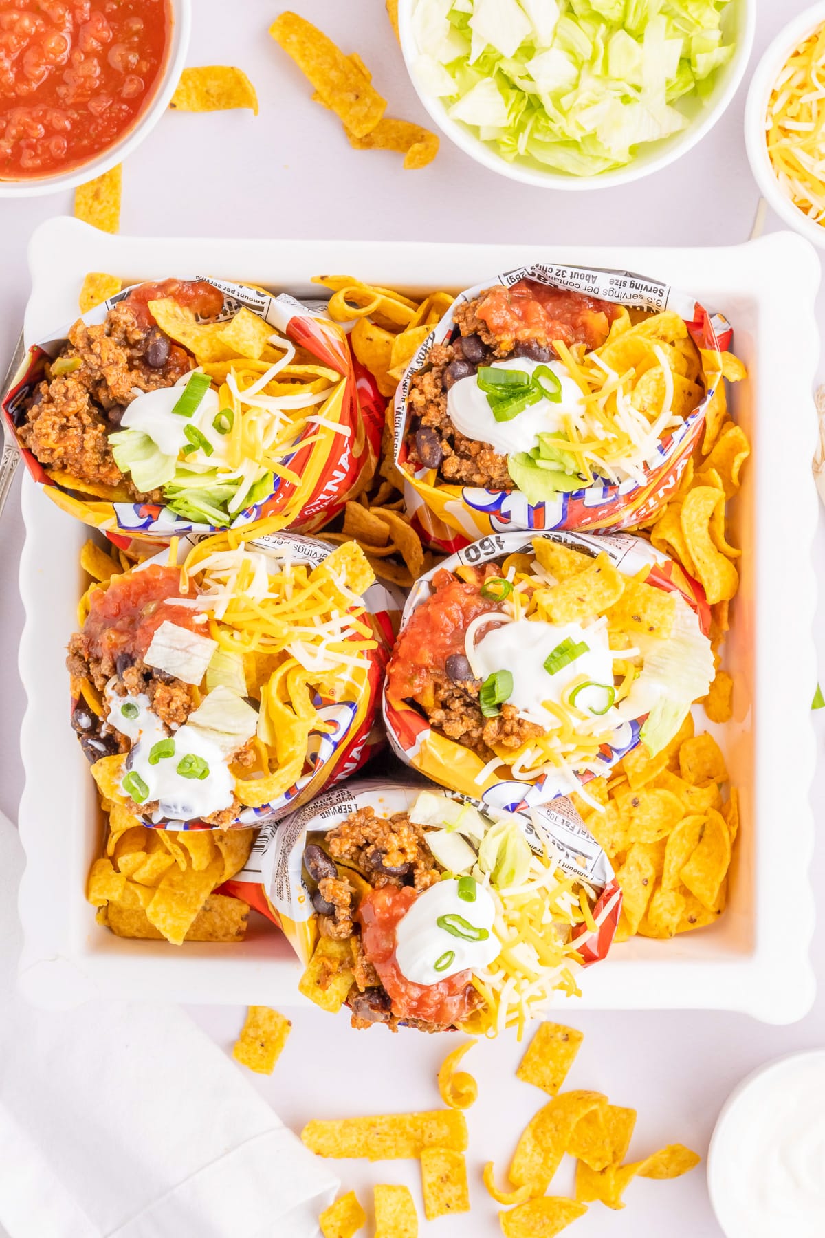 Overhead view of five bags of Frito corn chips all open in a tray from overhead full of taco toppings.