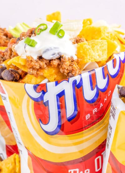 Square view of a single small bag of Fritos corn chips open on top and full of taco toppings.