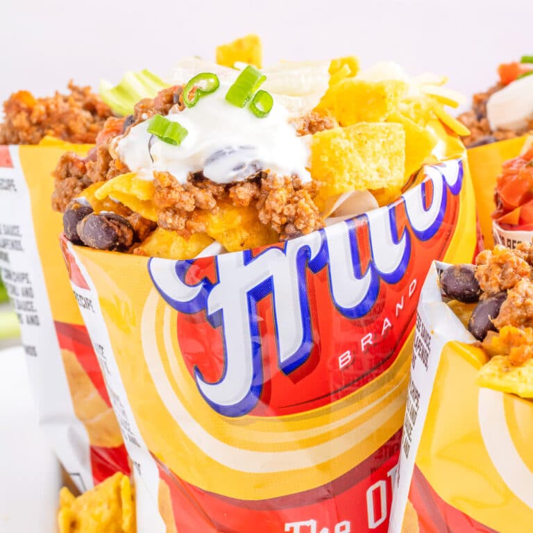 Square view of a single small bag of Fritos corn chips open on top and full of taco toppings.