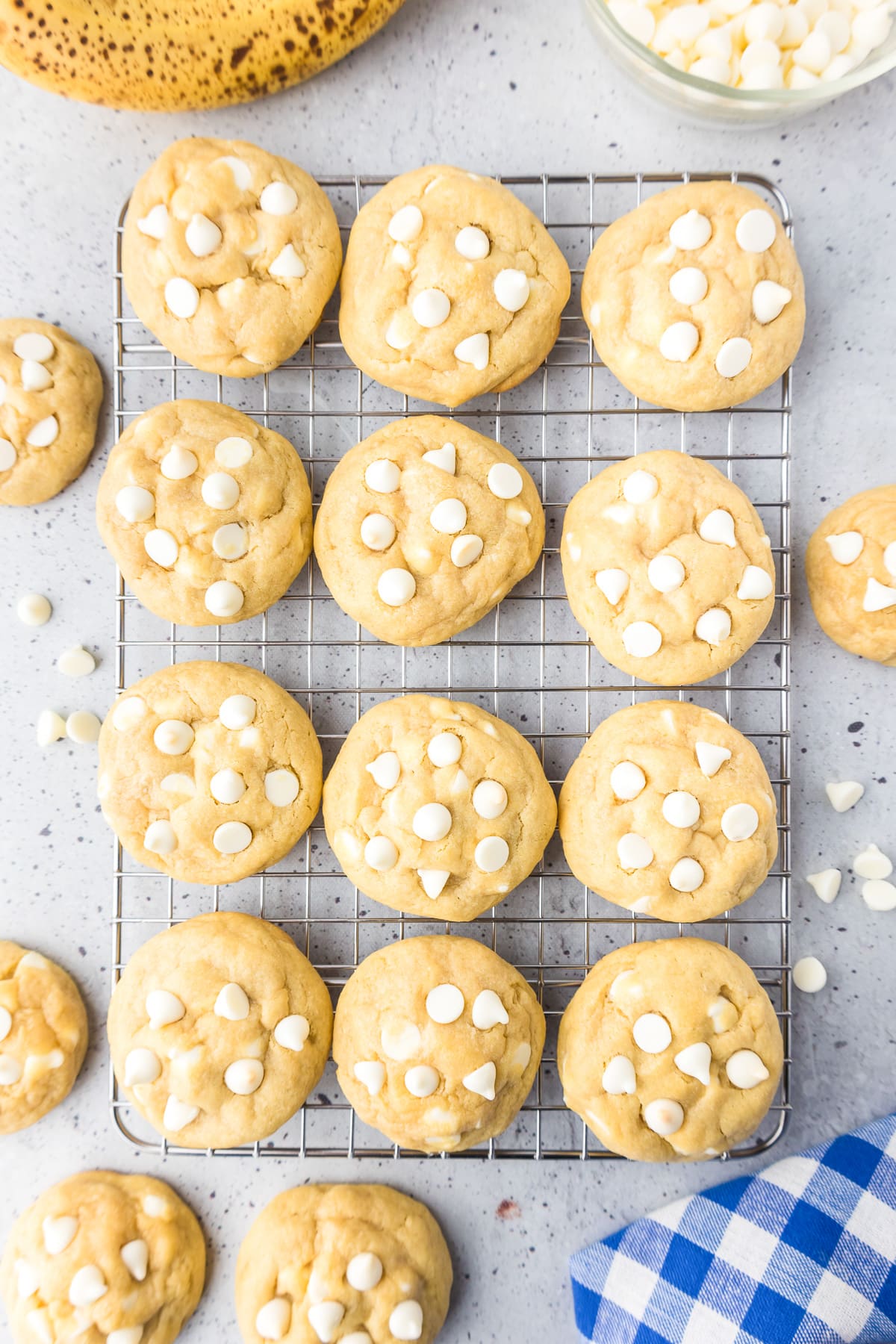 Banana pudding cookies topped with white chocolate chips on a wire cooling rack on a counter from above.