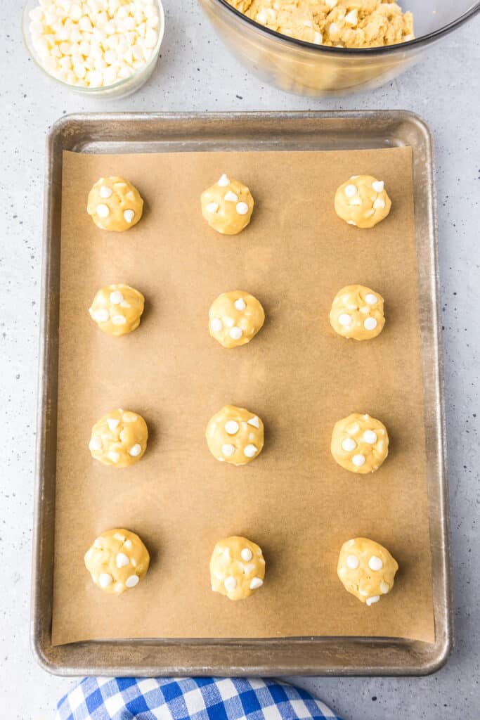Cookie dough balls topped with extra white chocolate chips spaced on a baking sheet.