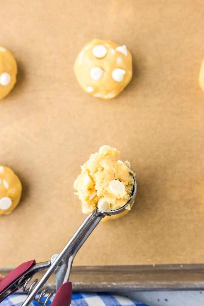 Cookie dough being scooped into balls with a metal scoop and added to a pan close up.