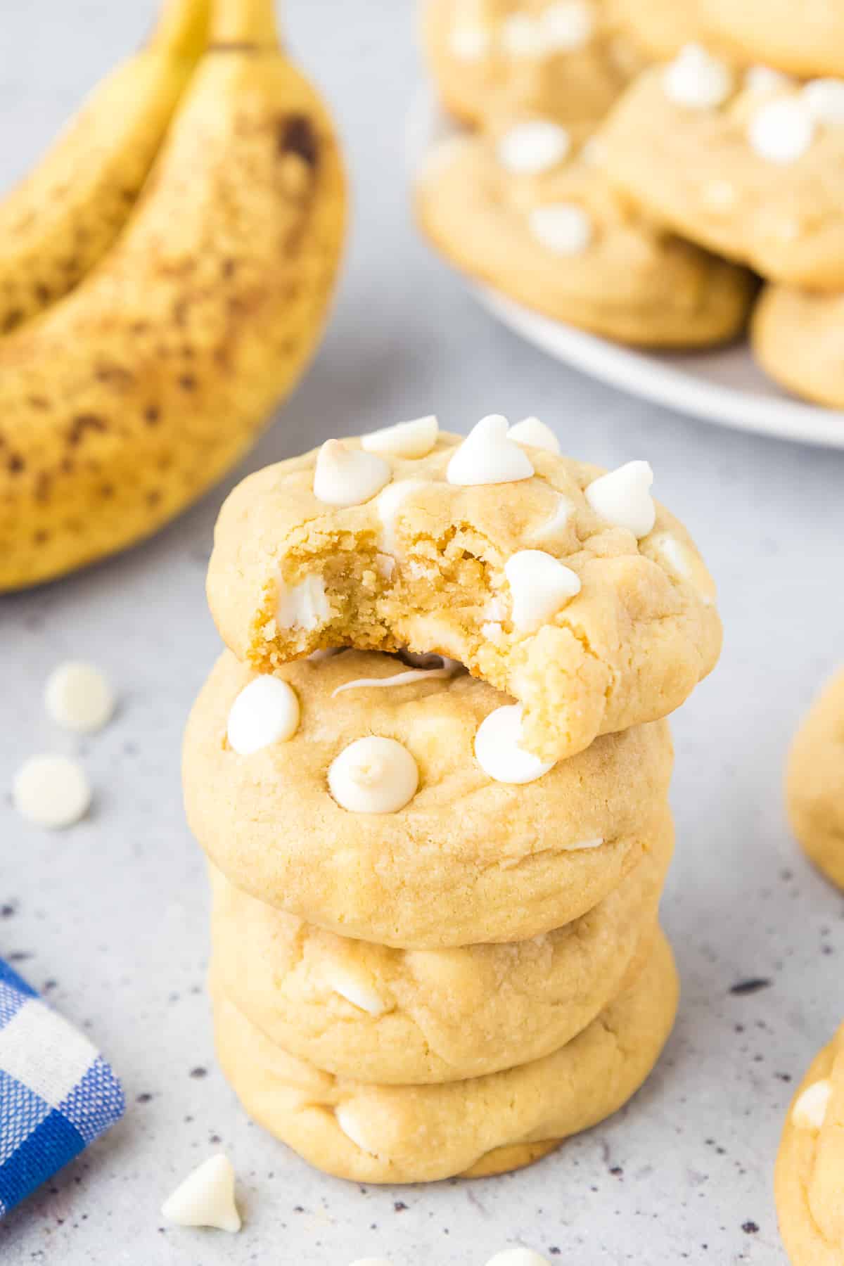 Stacked banana pudding cookies from the side topped with white chocolate chips with a bite missing from the top cookie.