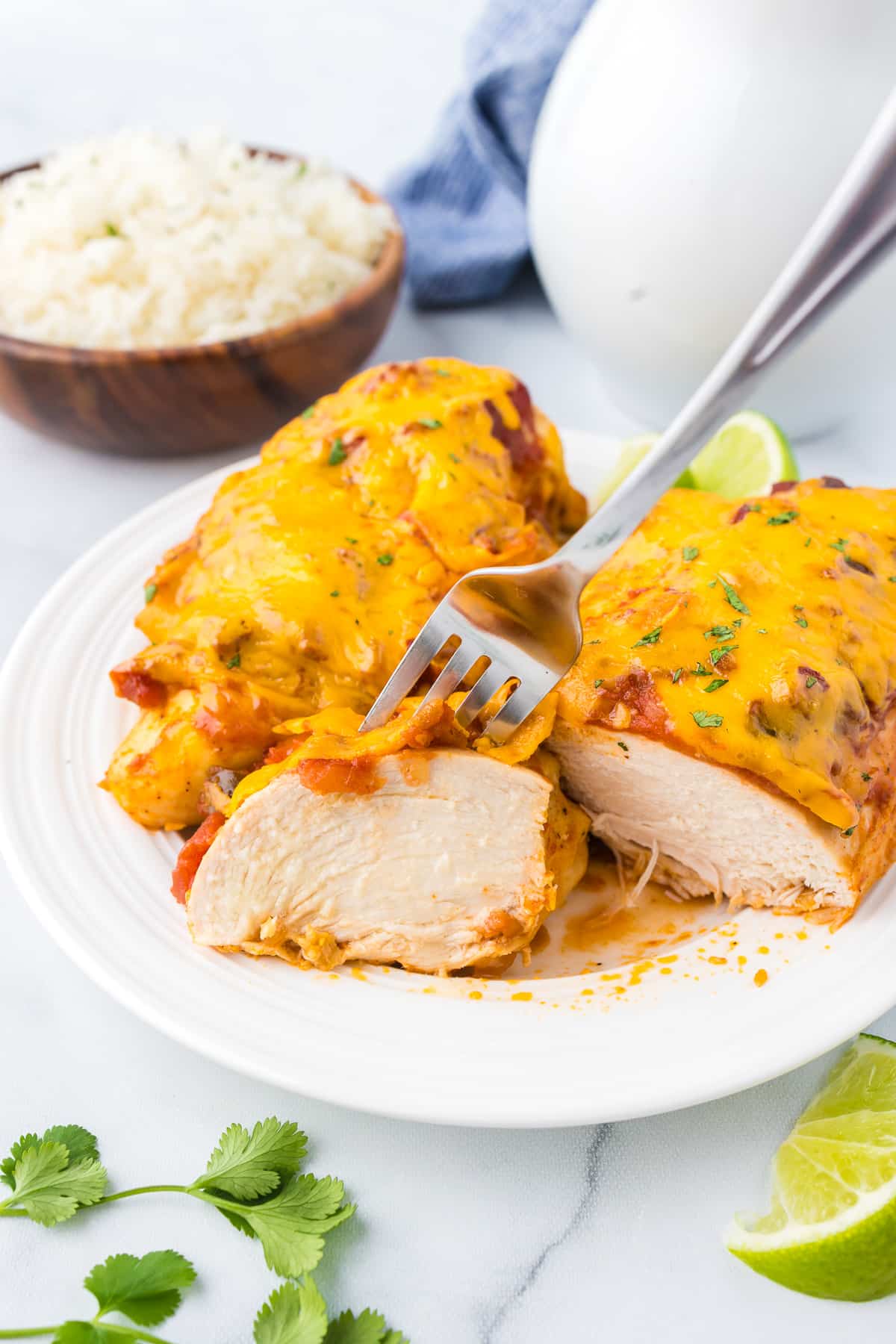 Two chicken breasts on a plate covered in cheese sliced open with a fork removing a piece.