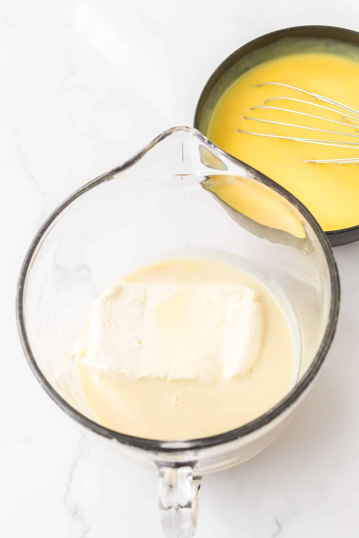 Cream cheese and sweetened condensed milk being mixed in a large bowl from overhead with banana pudding being mixed with a whisk in a bowl nearby.