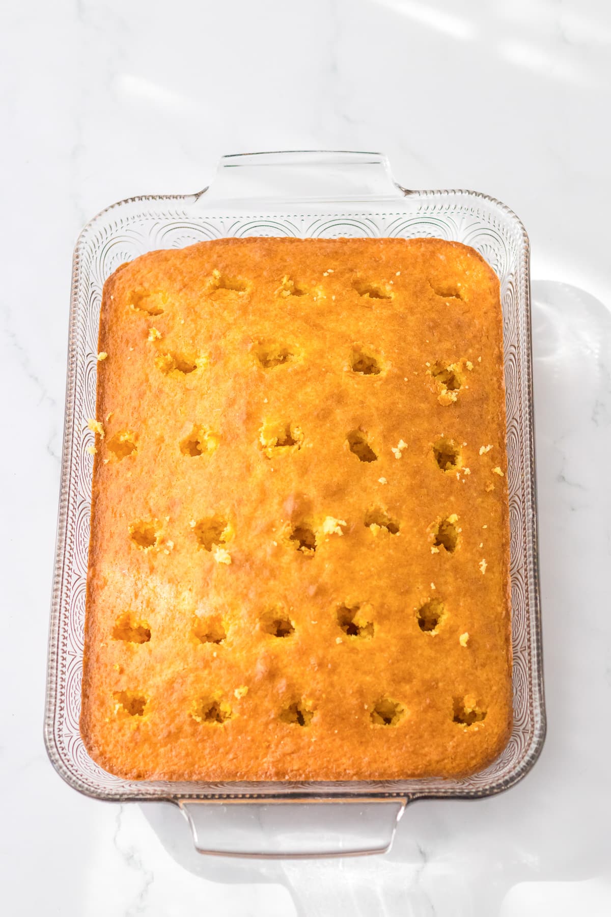 Yellow cake baked in a large rectangular pan with rows of holes poked in the cake.