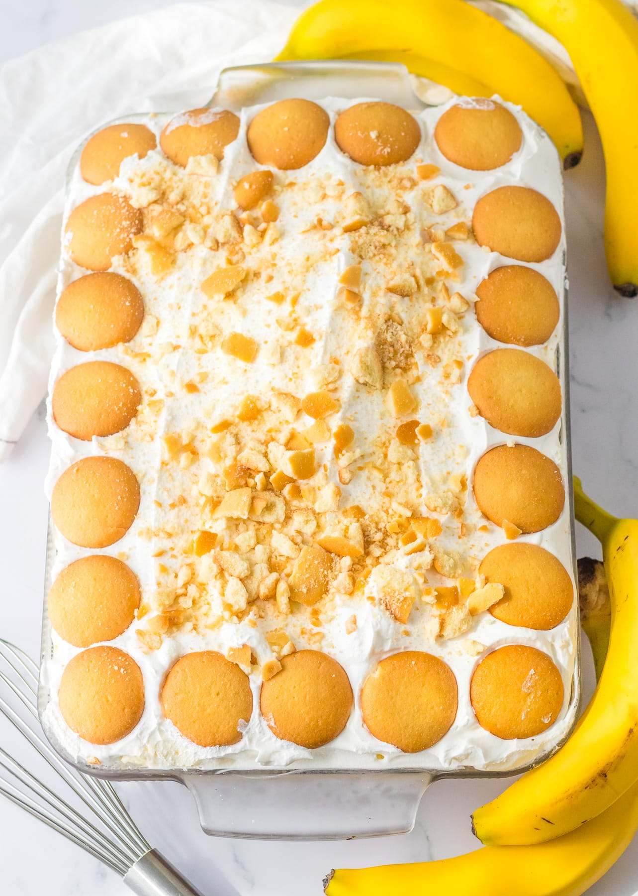 Banana pudding cake in pan from above topped with whipped topping and Nila Wafer cookies.