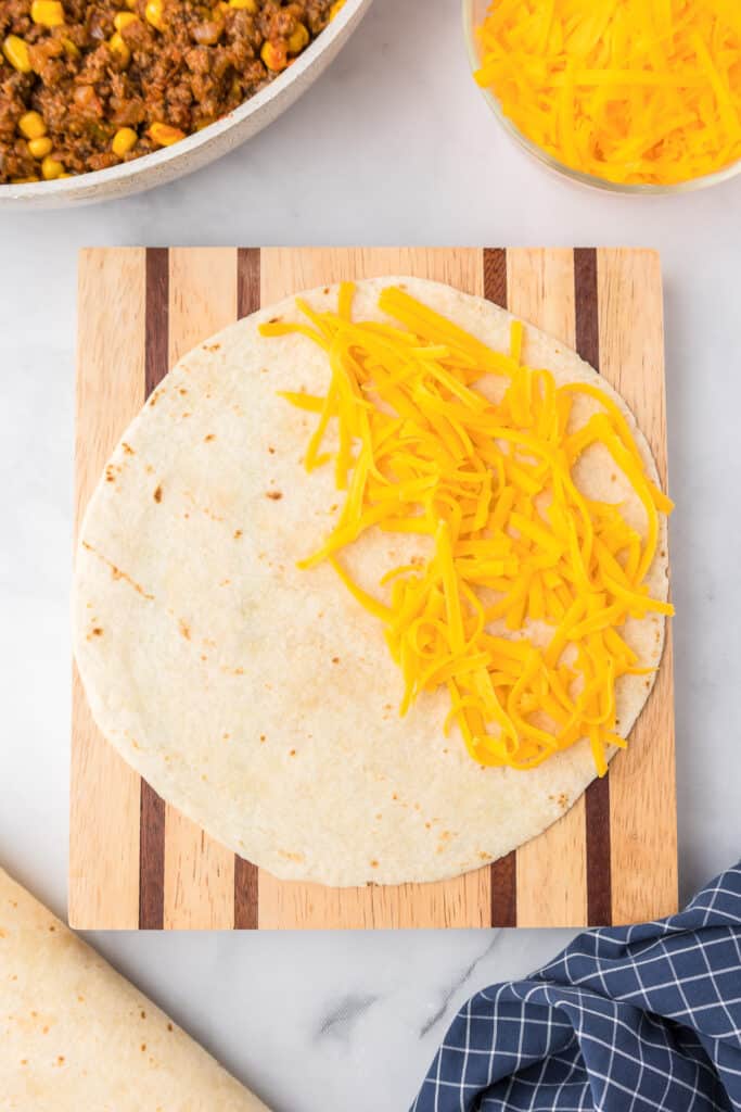 Tortilla on a cutting board with cheese on half of the quesadilla from above.