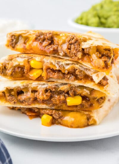 Side view of four quesadillas stacked on a plate from the side to show the beef, corn and cheesy filling.