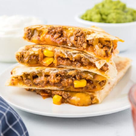 Side view of four quesadillas stacked on a plate from the side to show the beef, corn and cheesy filling.