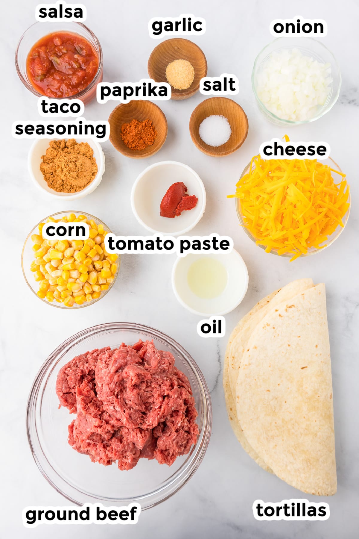 Ingredients for ground beef quesadilla in bowls from overhead on a counter with text labels.