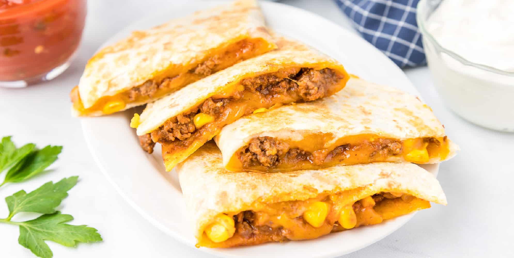 Wide view of cheesy beef quesadillas stacked and spread out on a platter.