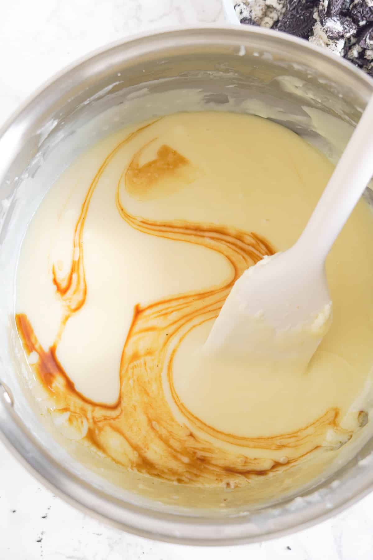 Vanilla being stirred into the white chocolate fudge mixture in a large pan from above.