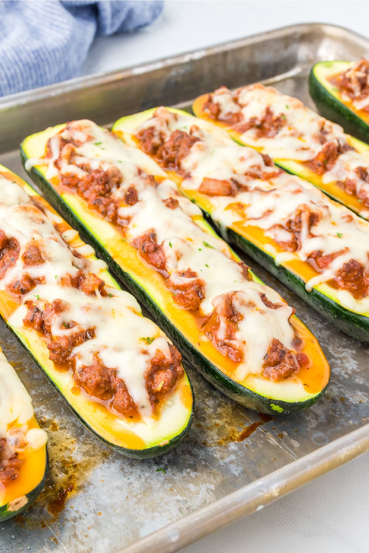 Stuffed zucchini boats full of italian ground beef and melted mozzarella cheese on a pan close up and at an angle.