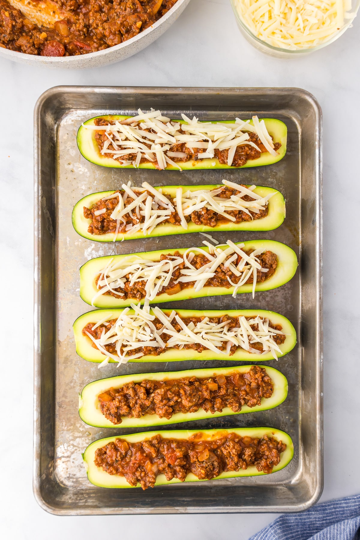 Stuffing hollowed out zucchini slices with italian ground beef and cheese from above on a pan.