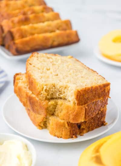 Slices of banana pineapple bread stacked on a plate with the top slice missing the bite and more slices in the background.