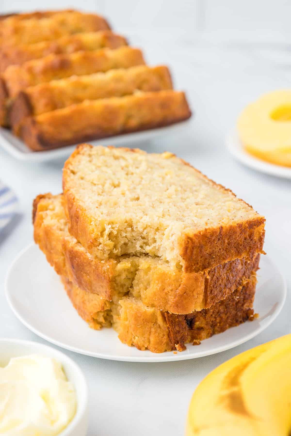 Slices of banana pineapple bread stacked on a plate with the top slice missing the bite and more slices in the background.