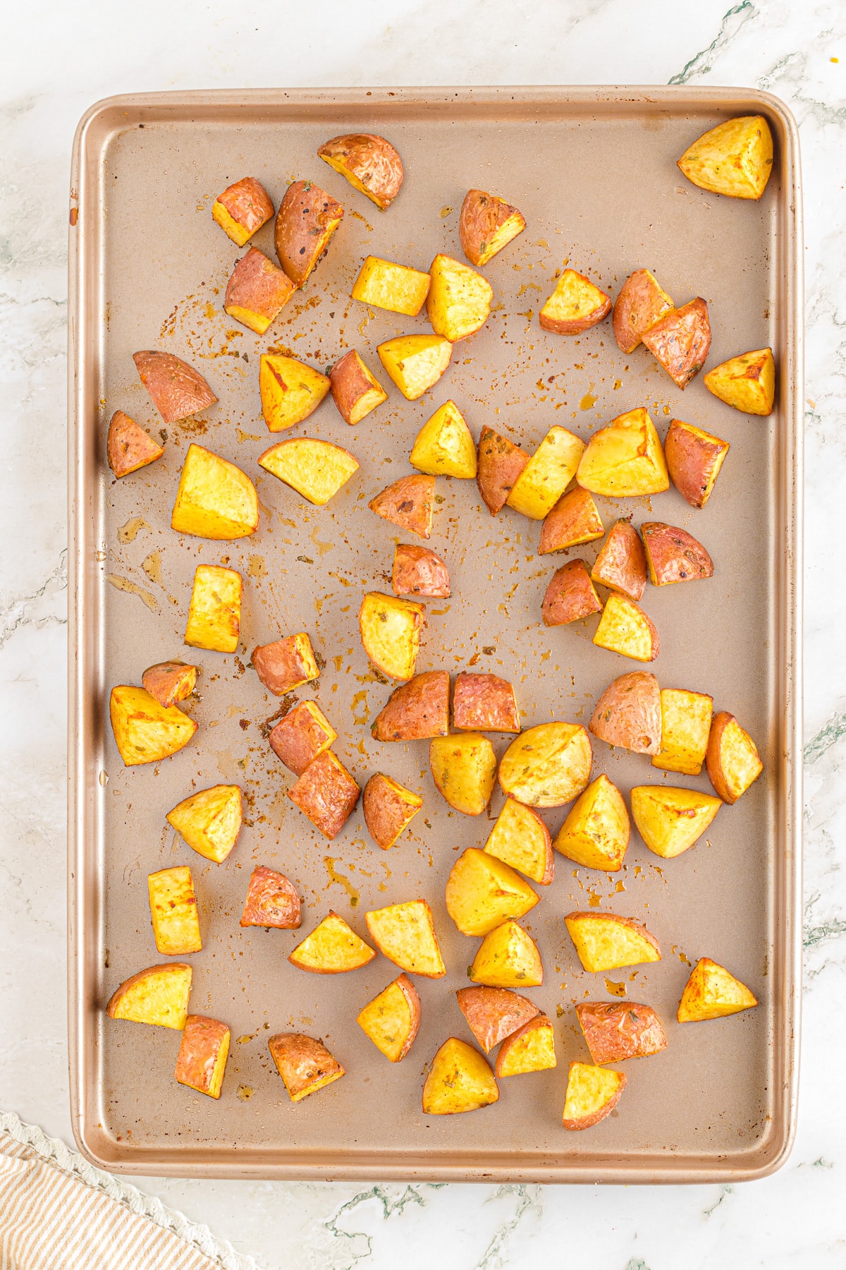 Partially roasted potatoes spread out on a sheet pan.